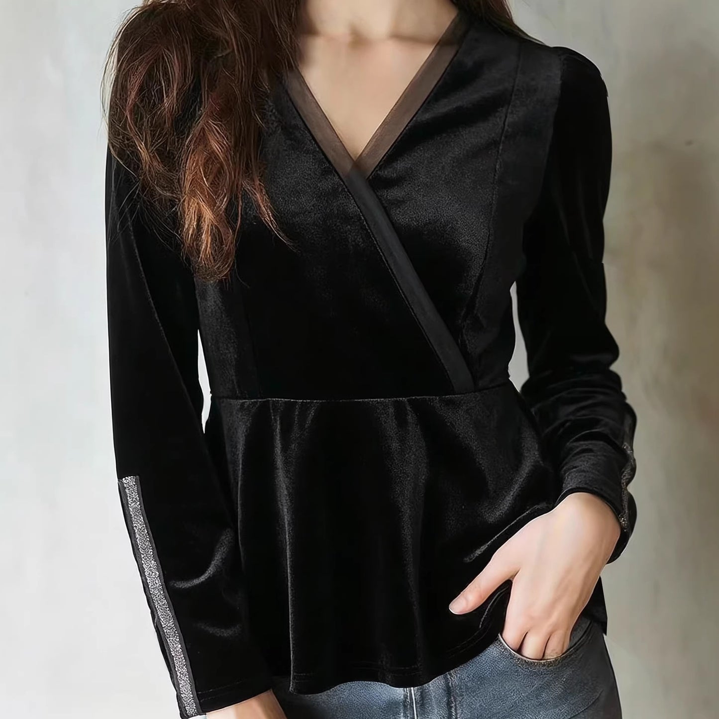 بلوزة مخملية سوداء بأكمام طويلة، بياقة على شكل حرف V، ضيقة عند الخصر، تُبرز جمال القوام.
